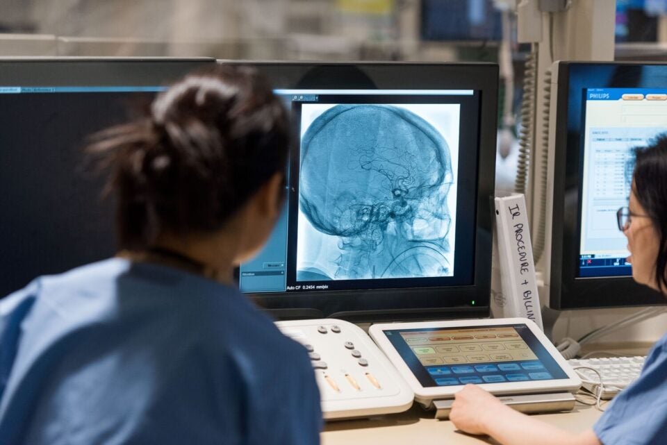 Two healthcare providers in scrubs look at a monitor showing a patient’s brain