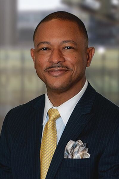 David Cook, MBA, is smiling in front of a blurred background while wearing a dark suit and yellow tie.