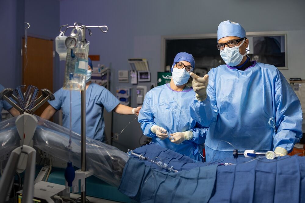 Sumon Roy, MD, interventional cardiologist at BMC South, stands in full surgical scrubs and mask over an operating table during a cardiac procedure