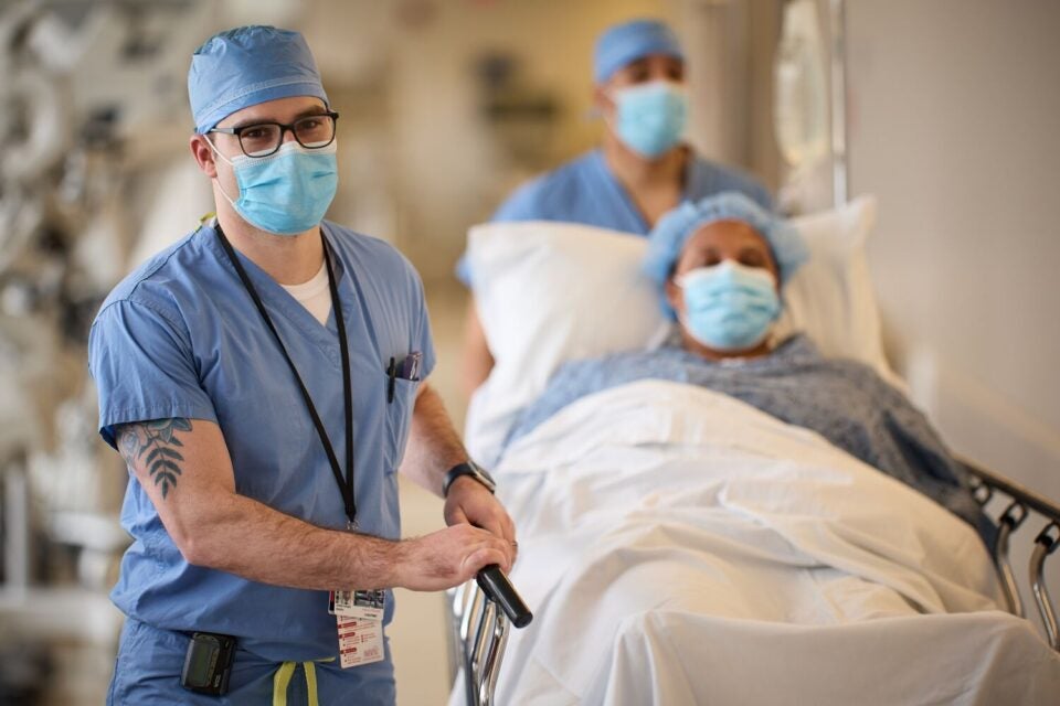 Christopher Digesu, MD, thoracic surgeon at BMC Health System, escorts a patient in a hospital bed down a hallway