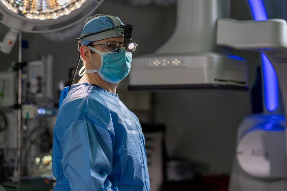 BMC Brighton vascular surgeon Scott Prushik, MD, stands in an operating theater wearing full scrubs, cap, mask, and a headlamp