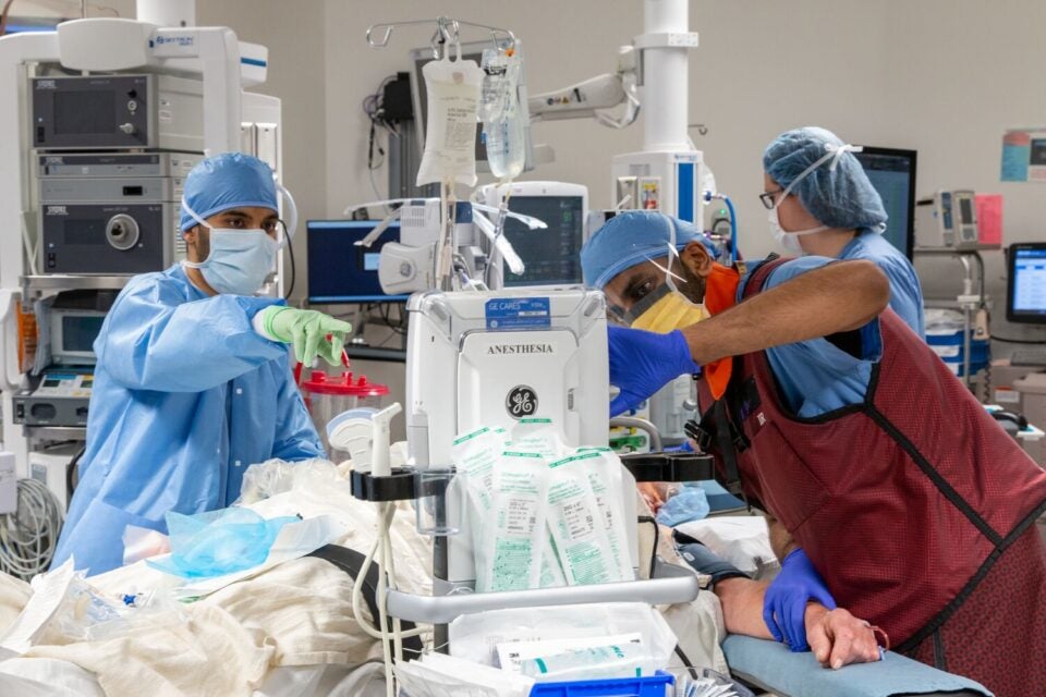 A scrubbed-in, masked, and capped member of a surgical team checks a monitor during a surgical procedure