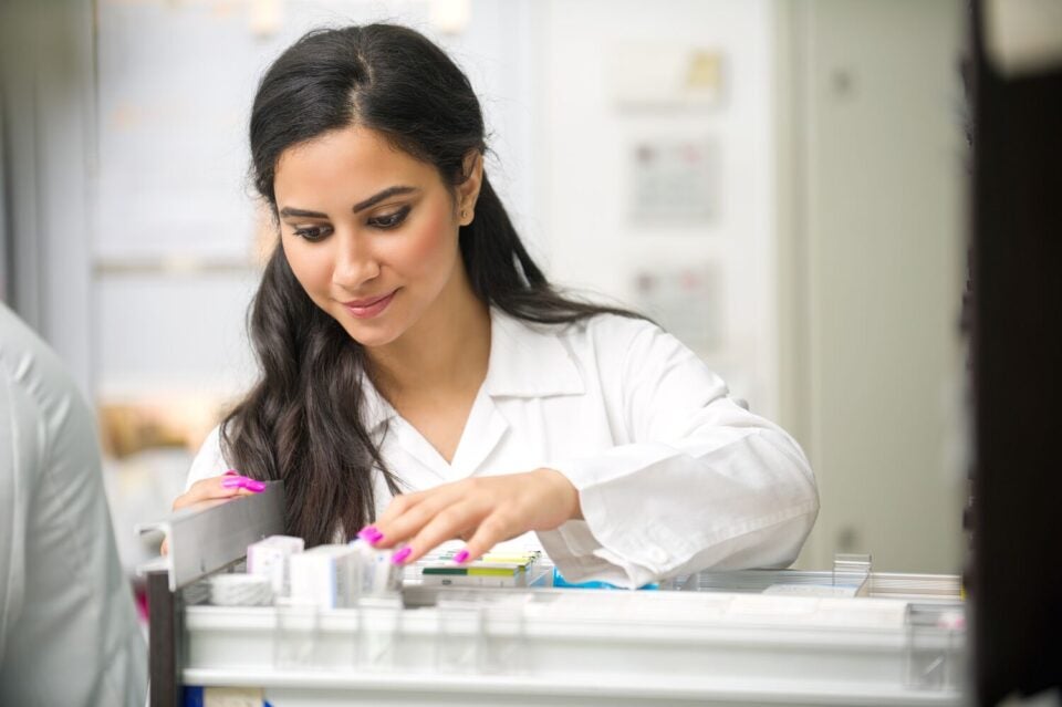 Woman in a white lab coat looking through a tray of prepared prescriptions