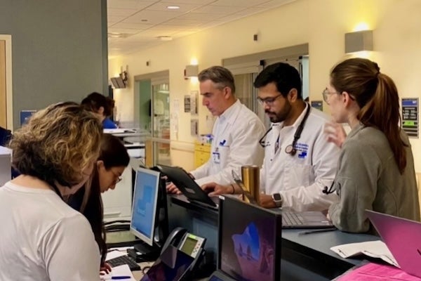 Candid photo of pulmonary and critical care medicine fellows leaning over paperwork and computers at the unit station