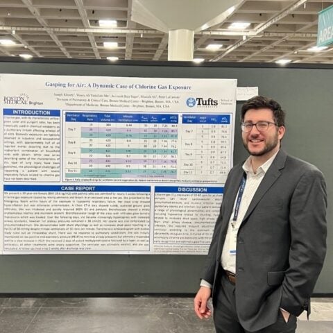 A pulmonary and critical care medicine fellows stands next to his research poster