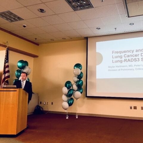 A pulmonary and critical care medicine fellow presents research standing at a podium in front of a screen
