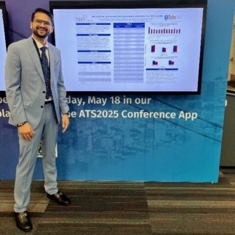 A pulmonary and critical care medicine fellow proudly stands next to his poster presentation