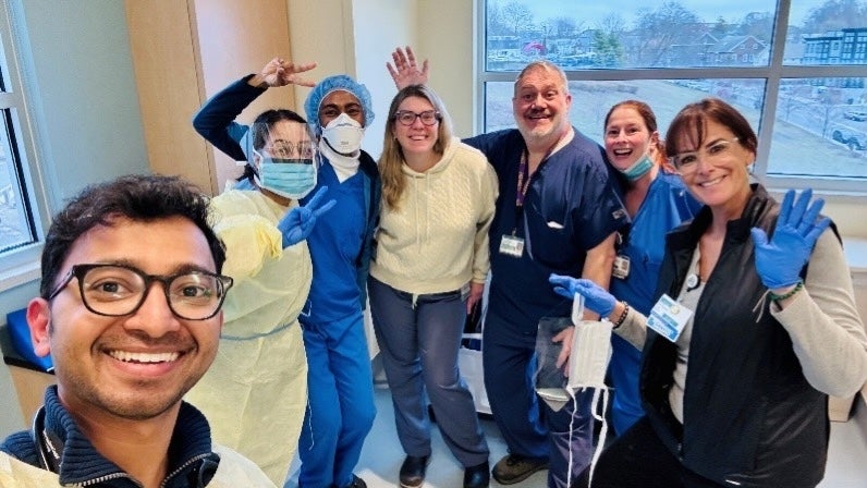 A group of pulmonary and critical care medicine fellows and staff smile and wave in a hallway
