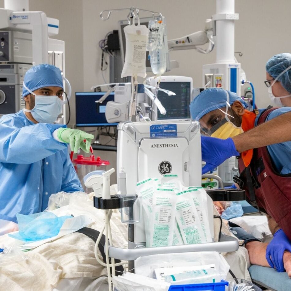 A scrubbed-in, masked, and capped member of a surgical team checks a monitor during a surgical procedure (1x1 crop)