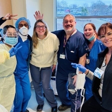 A group of pulmonary and critical care medicine fellows and staff smile and wave in a hallway (1x1 crop)