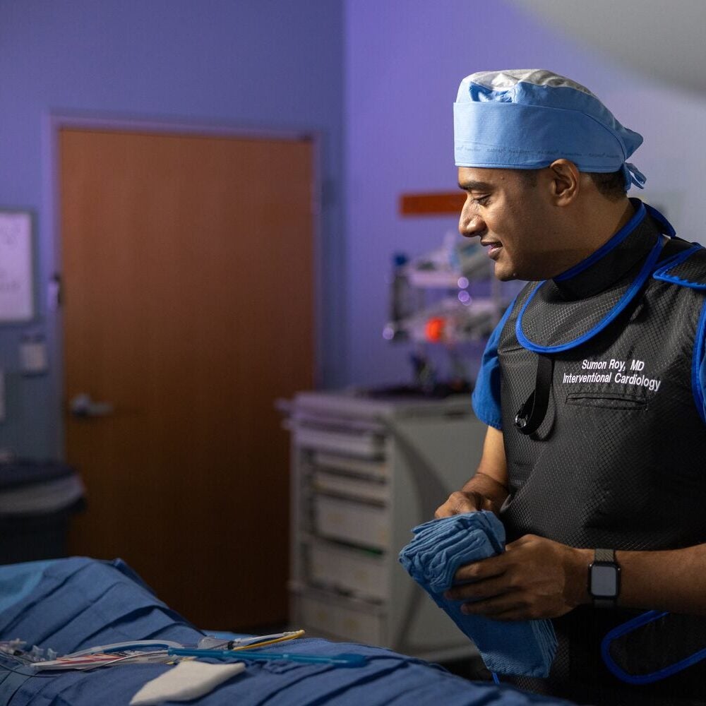 Sumon Roy, MD, interventional cardiologist at BMC South, stands over an operating table looking at an array of surgical instruments and tools.